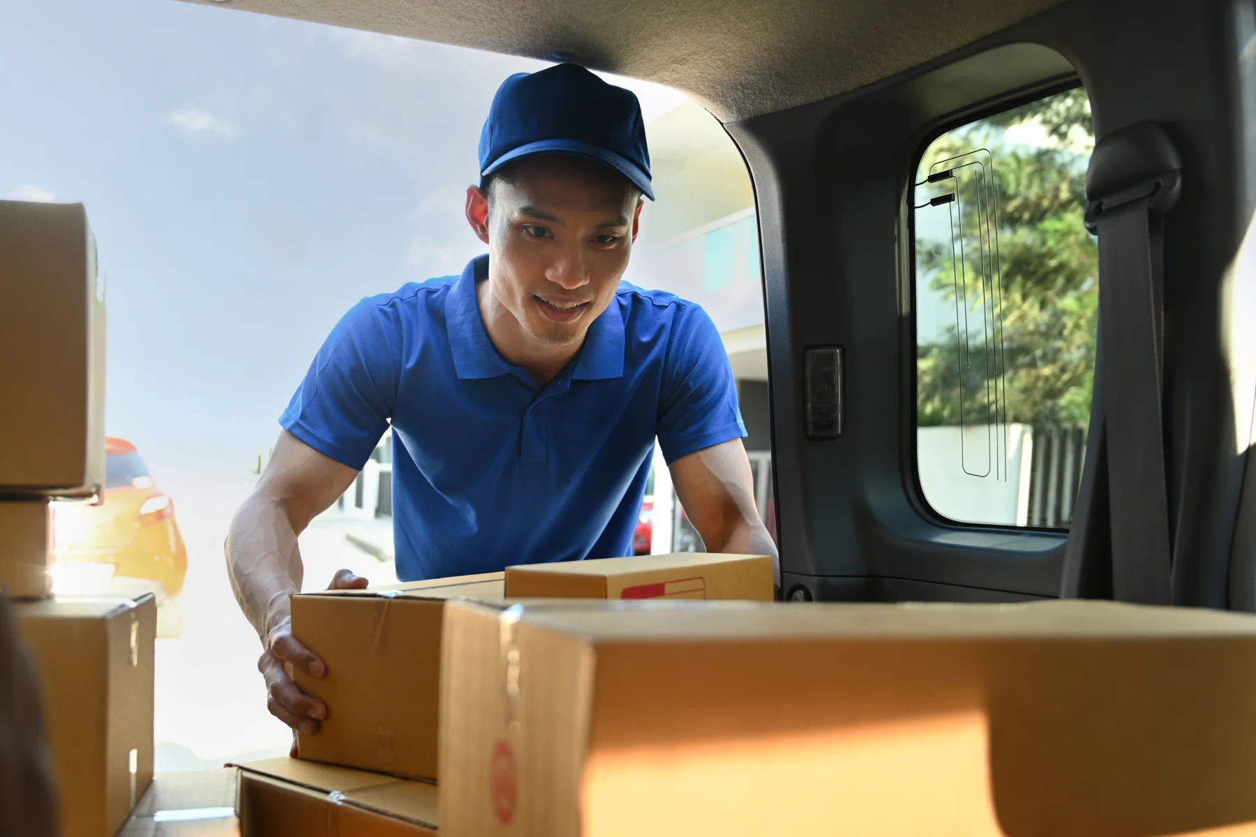 Delivery worker loading cardboard packages into the back of a van for last-mile shipping