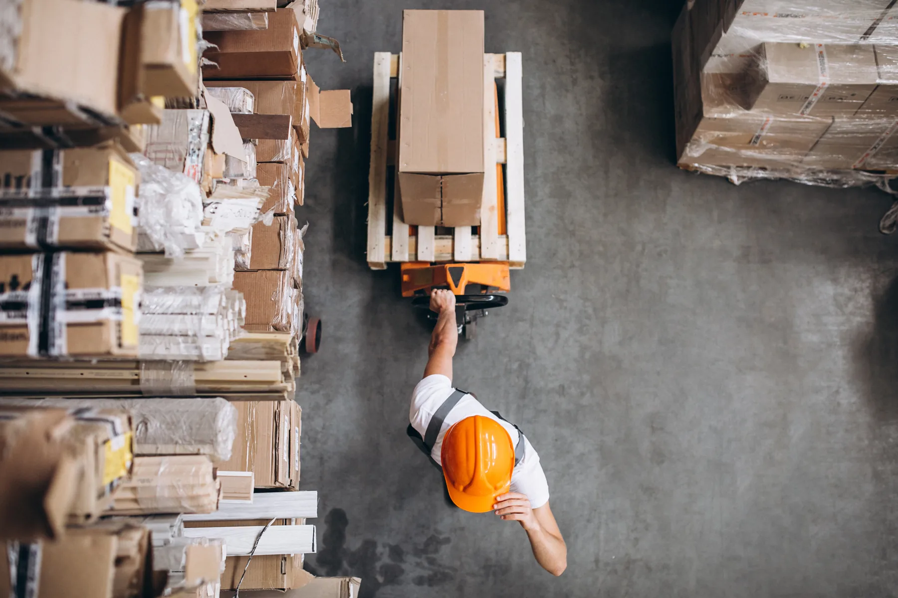 Overhead view of warehouse pallets, stacked boxes, and a worker managing inventory with pallet equipment